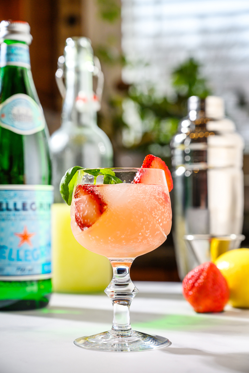 Photo of Strawberry Limoncello Fizz Cocktail with strawberry basil simple syrup, fresh strawberries, lemon juice with a basil garnish in a glass of ice.